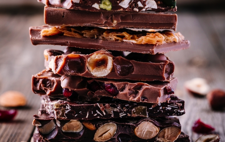 Stapel Vollmilch- und Zartbitterschokolade mit Nüssen, Karamell und Früchte und Beeren auf Holzhintergrund  - © nblxer - stock.adobe.com