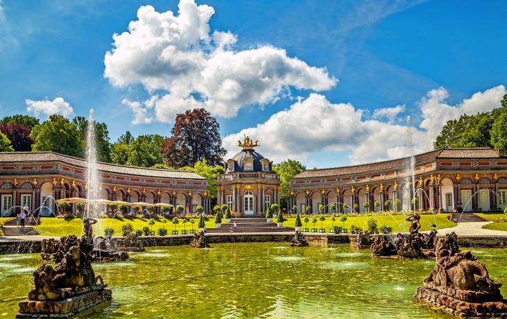 Barockgarten mit Springbrunnen und historischem Gebäude im Hintergrund. - © pure-life-pictures - stock.adobe.com