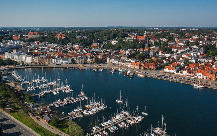 Luftaufnahme eines Hafens mit Segelbooten und Stadtsilhouette im Hintergrund. - © a_medvedkov - stock.adobe.com