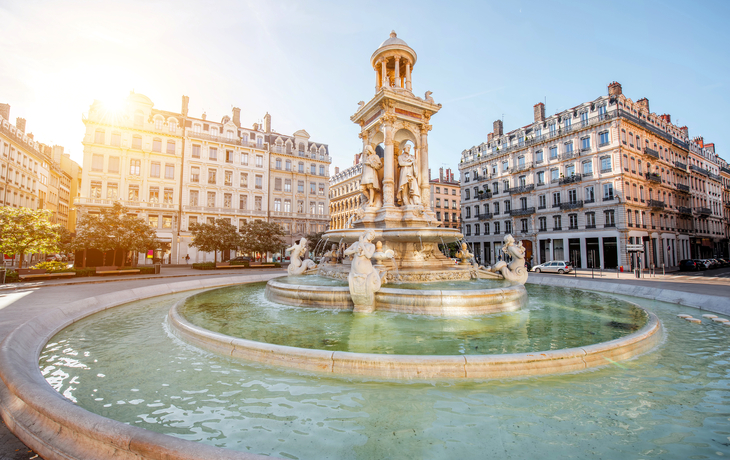Brunnen auf einem Platz mit historischen Gebäuden im Hintergrund bei Sonnenschein. - © rh2010 - stock.adobe.com