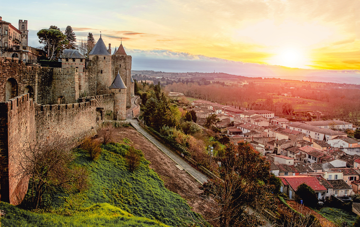 Mittelalterliche Burg bei Sonnenuntergang mit angrenzendem Dorf und Landschaft. - ©steftach - stock.adobe.com