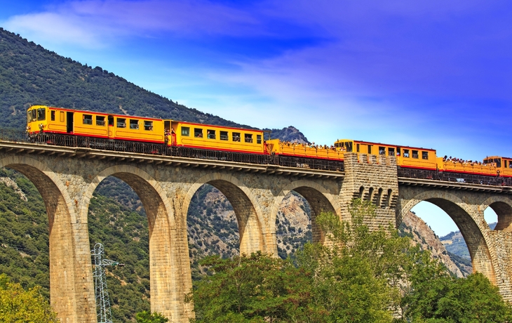 Gelber Zug überquert ein hohes Steinviadukt in einer bergigen Landschaft. - © Charles LIMA - stock.adobe.com