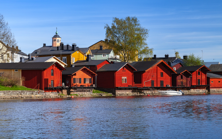 Rote Holzhäuser am Flussufer mit blauem Himmel. - © evannovostro - stock.adobe.com