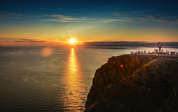 Personen bei Sonnenuntergang am Nordkap mit Globus-Skulptur. - © RuZi - stock.adobe.com