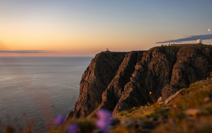 Personen bei Sonnenuntergang am Nordkap mit Globus-Skulptur. - © RuZi - stock.adobe.com