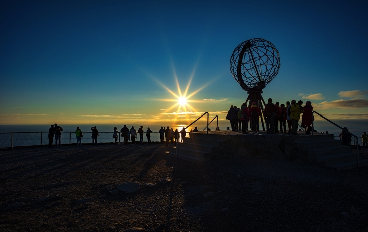 Personen bei Sonnenuntergang am Nordkap mit Globus-Skulptur. - © RuZi - stock.adobe.com