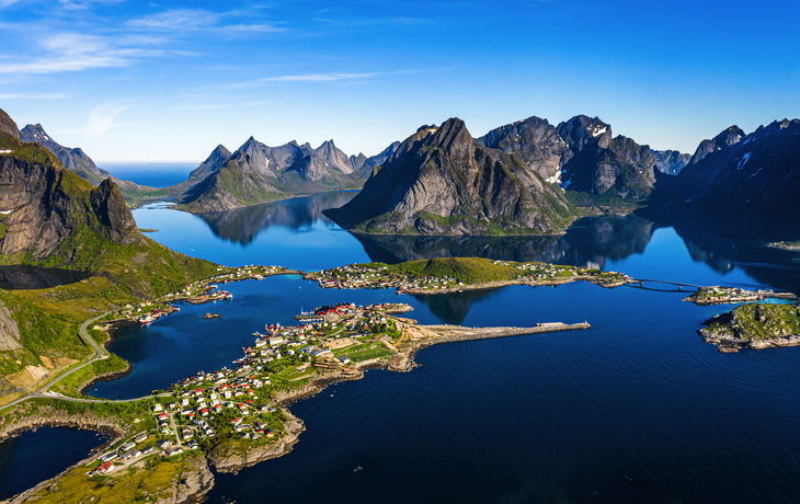Rote Holzhäuser am Fjord mit Bergen im Hintergrund unter blauem Himmel - © Jamo Images - stock.adobe.com