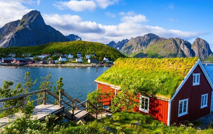 Rote Holzhäuser am Fjord mit Bergen im Hintergrund unter blauem Himmel - © Jamo Images - stock.adobe.com