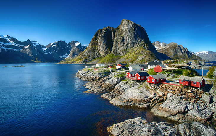 Rote Holzhäuser am Fjord mit Bergen im Hintergrund unter blauem Himmel - © Jamo Images - stock.adobe.com