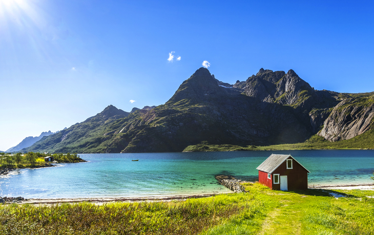 Rote Holzhäuser am Fjord mit Bergen im Hintergrund unter blauem Himmel - © Jamo Images - stock.adobe.com