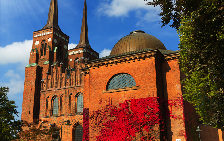 Rotes Backsteingebäude hinter blühenden Rosen im Vordergrund. - ©Michael Runkel/Danita Delimont - stock.adobe.com
