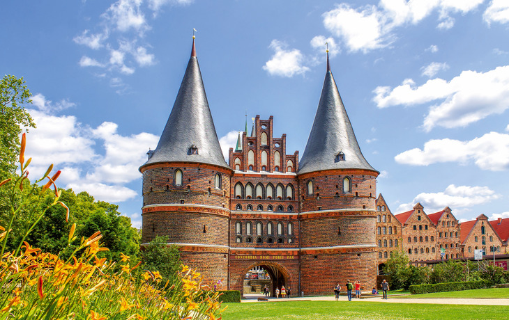 Backstein-Tor mit zwei Türmen, blauer Himmel, Blumen im Vordergrund. - © pure-life-pictures - Fotolia