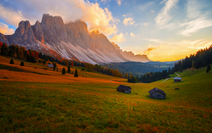 Berglandschaft mit Hütten bei Sonnenuntergang, Dolomiten im Hintergrund. - © rolandbarat - stock.adobe.com