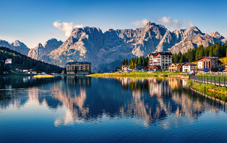 Berglandschaft mit Hütten bei Sonnenuntergang, Dolomiten im Hintergrund. - © rolandbarat - stock.adobe.com
