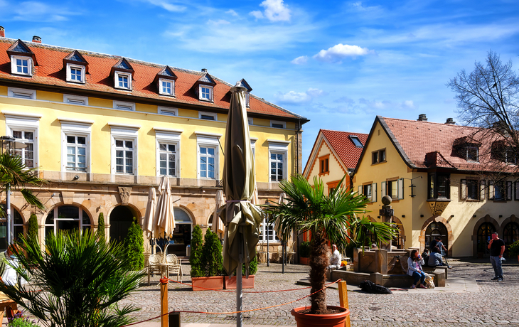 Historischer Platz mit gelben Gebäuden, Sonnenschirmen und Palmen bei klarem Himmel. - © EKH-Pictures - stock.adobe.com