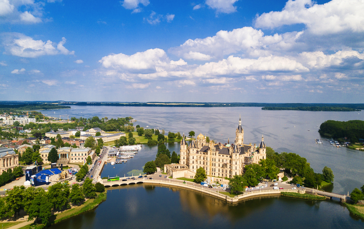Luftaufnahme eines Schlosses am Wasser unter blauem Himmel und Wolken. - © SEB - www.sebfoto.de - stock.adobe.com